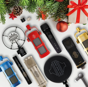 various sontronics microphones lying on a white background with christmas tree foliage, pine cone, bauble and christmas present across the top of the picture